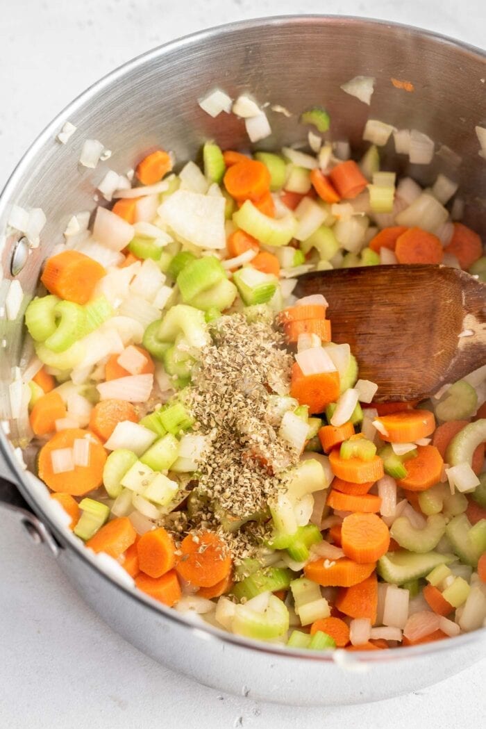 Onions, carrot, celery, dried herbs and garlic in a soup pot with a wooden spoon.