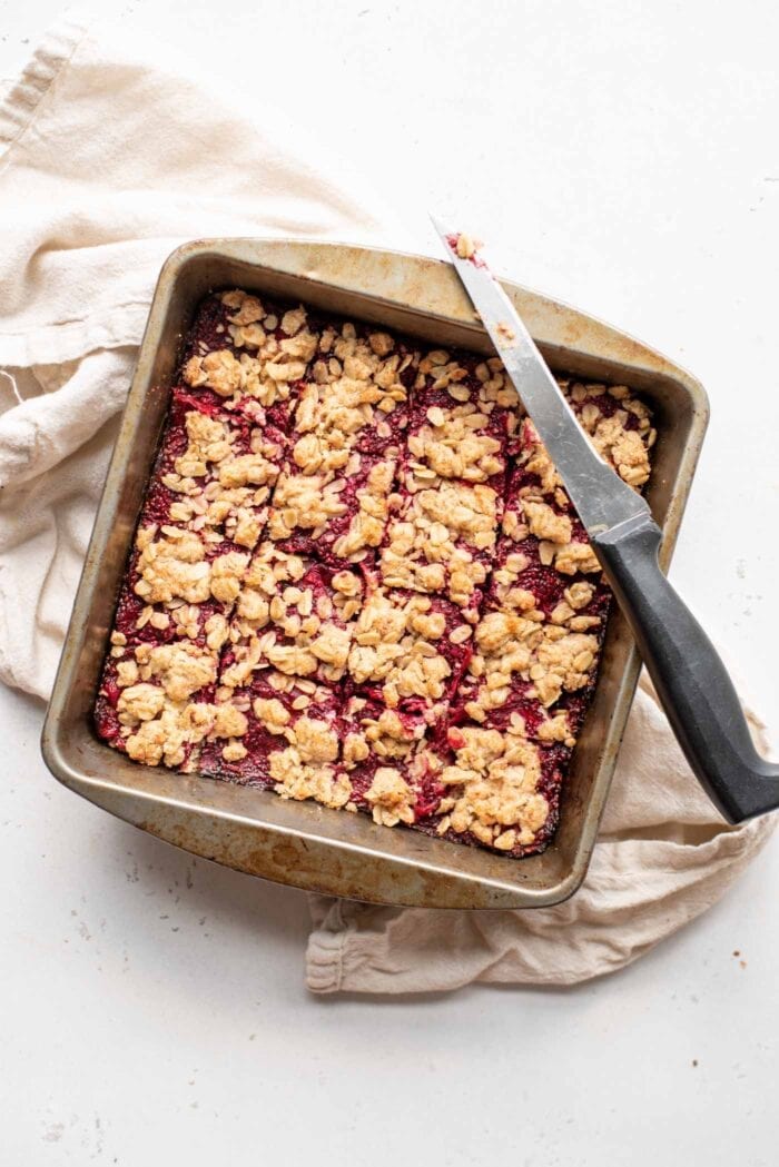 A pan of cranberry oatmeal bars sliced into 16 portions with a knife resting on the edge of the pan.