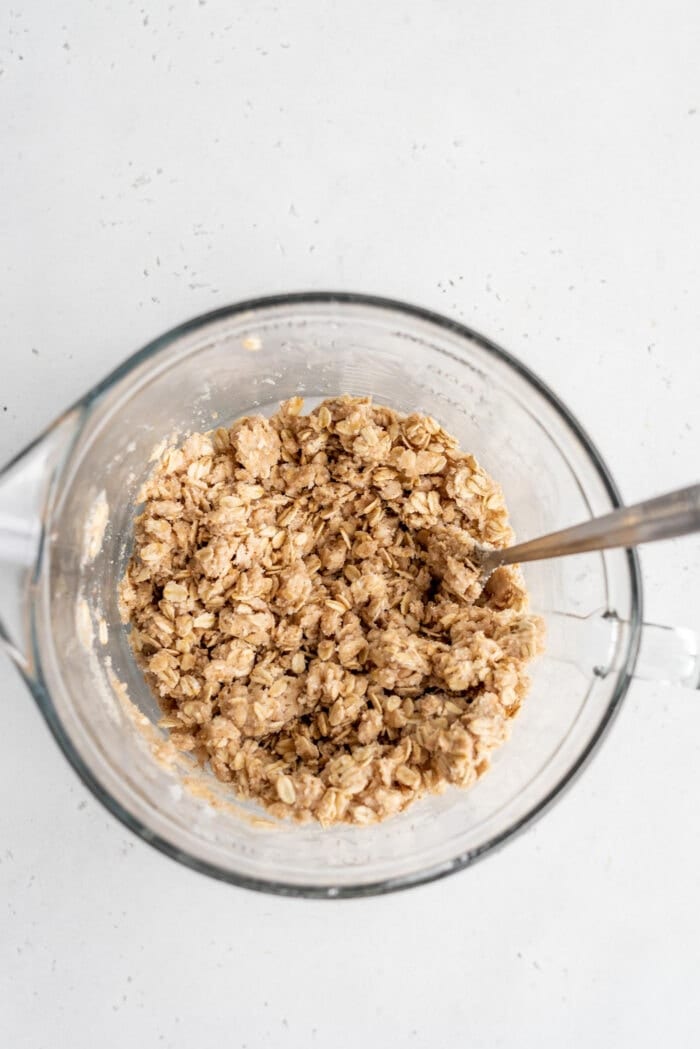 Raw oat crumble in a mixing bowl with a spoon.