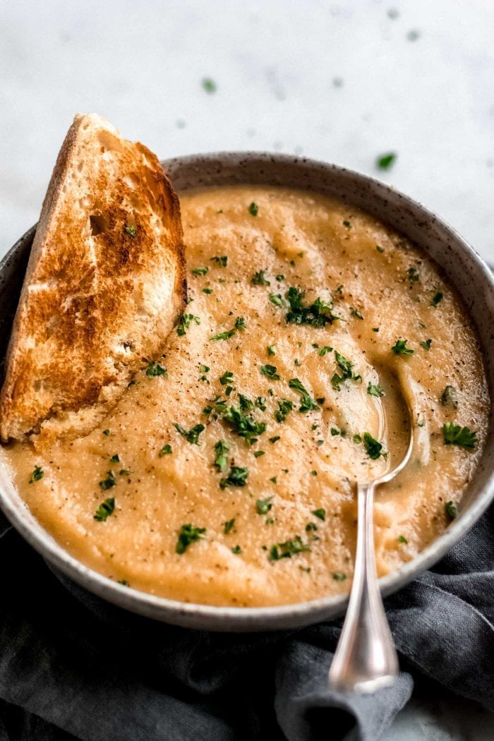 Creamy roasted garlic cauliflower soup in a bowl with parsley and fresh bread.