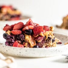 Baked oatmeal topped with berries on a plate with a spoon, two additional plates in background.