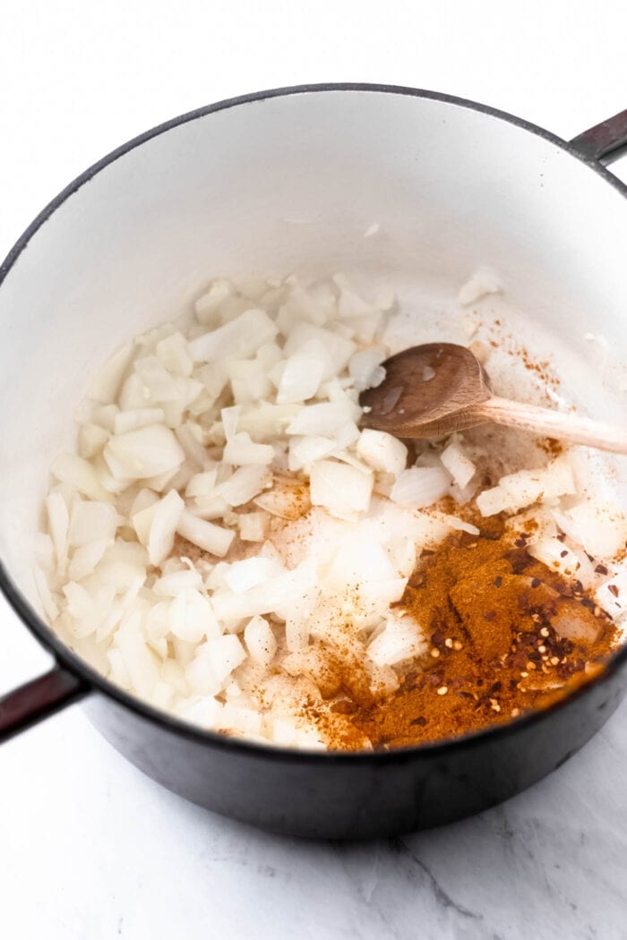 Chopped onion, minced garlic and curry powder cooking in a large soup pot with a wooden spoon.