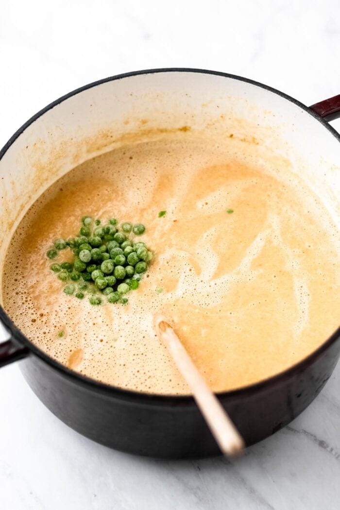 Green peas being stirred into soup in a stock pot.