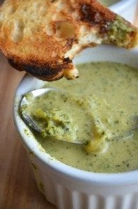 A piece of bread being dipped into a small bowl of broccoli soup.
