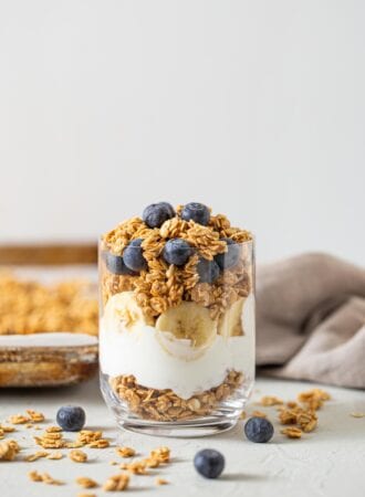 Yogurt, banana and granola parfait topped with blueberries in a glass jar.