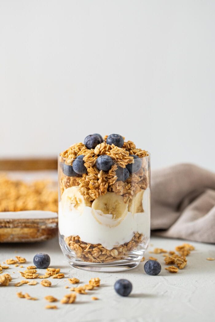 Yogurt, banana and granola parfait topped with blueberries in a glass jar.