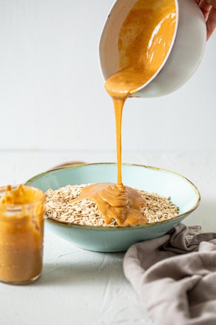 Peanut butter being poured over a bowl of oats.