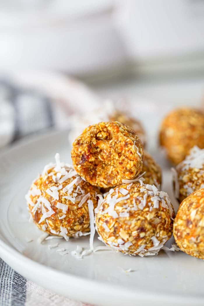 A carrot energy ball with a bit taken out of it on a plate.