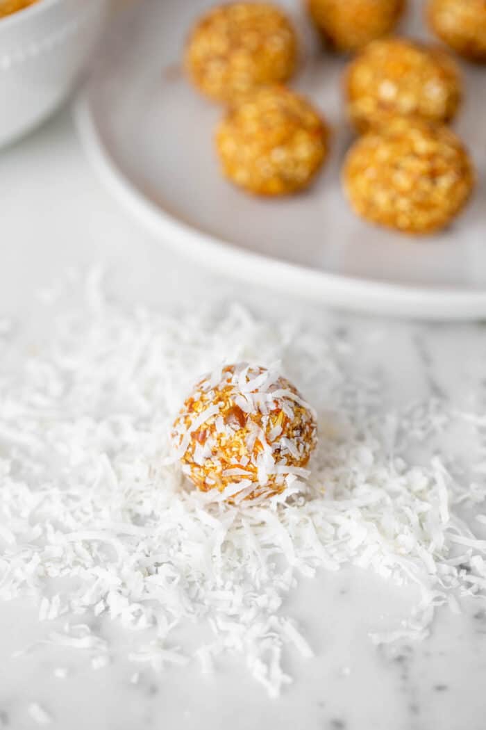 An energy ball being rolled in shredded coconut on a counter top.