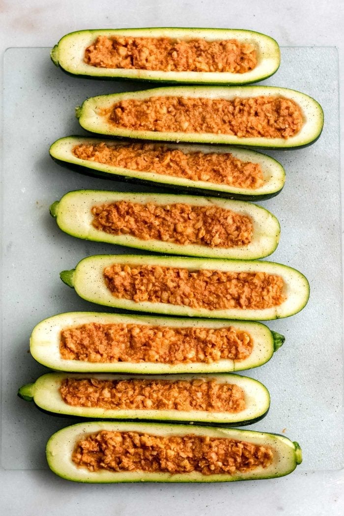 Chickpea stuffed zucchini boats ready to go in the oven on a baking tray lined with parchment paper.