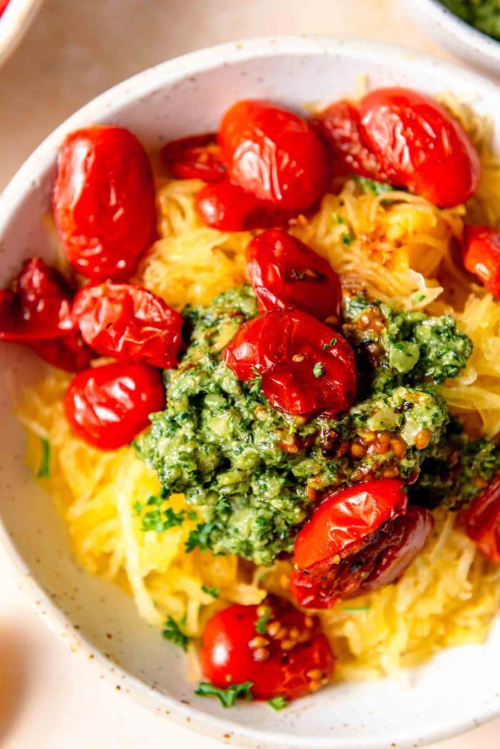 Bowl of spaghetti squash noodles topped with basil pesto sauce and tomatoes.