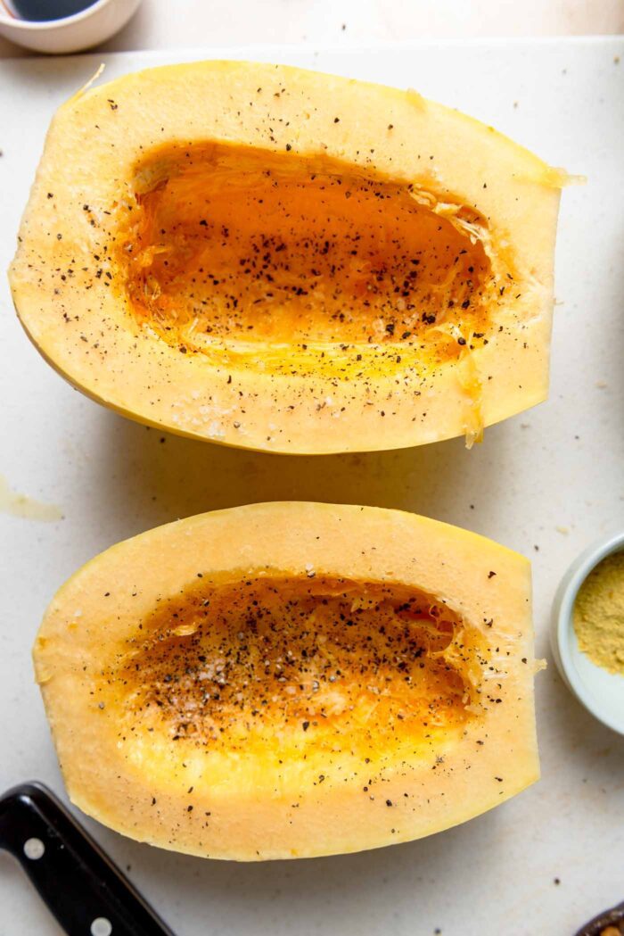 Two halves of a spaghetti squash sprinkled with salt and pepper.