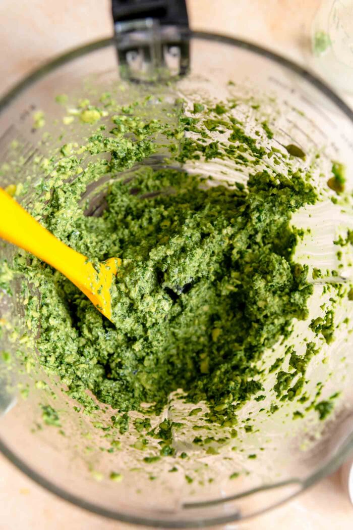 Pesto in a food processor container with a small spatula resting in it.