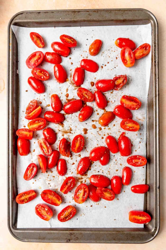 Chopped tomatoes tossed in herbs and balsamic vinegar on a baking sheet.