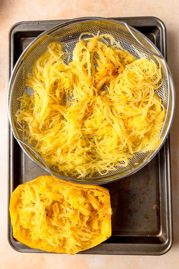 Spaghetti squash noodles in a colander on a baking sheet.