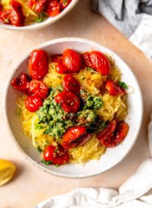Bowl of spaghetti squash topped with pesto and roasted tomatoes.