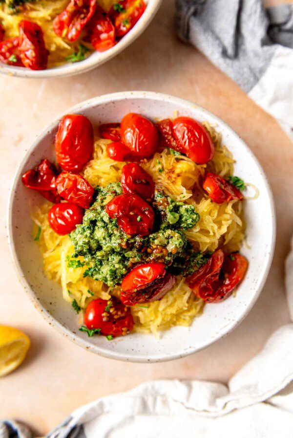 Bowl of spaghetti squash topped with pesto and roasted tomatoes.