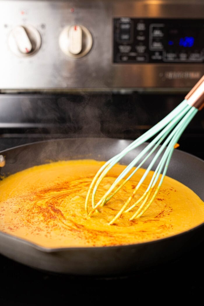 Creamy pumpkin pasta sauce being stirred with a whisk a skillet on the stovetop.