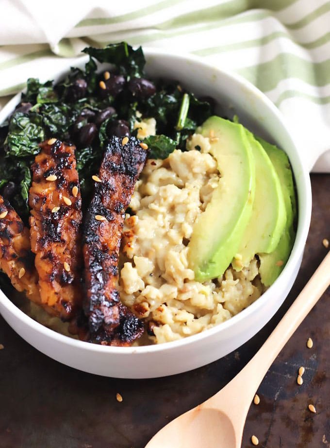 A bowl of oats topped with kale, avocado and tempeh.