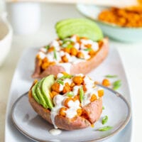 Sweet potato stuffed with buffalo chickpeas and avocado, topped with white sauce.