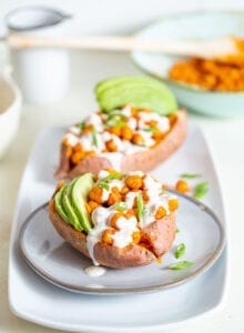Sweet potato stuffed with buffalo chickpeas and avocado, topped with white sauce.