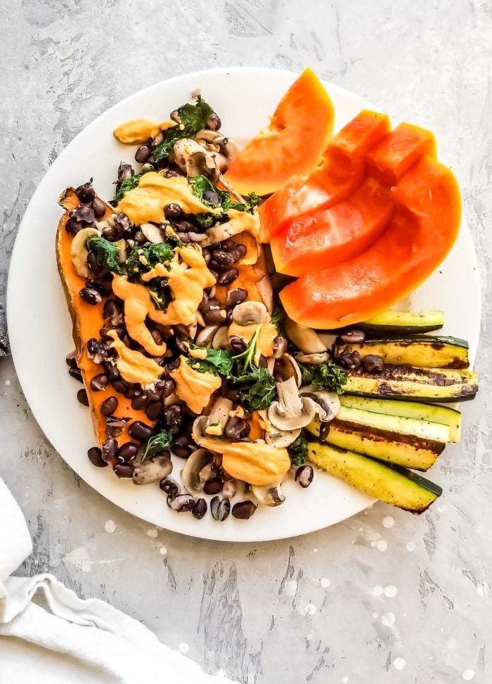 A plate of sweet potato topped with mushrooms and black beans with slices of papaya.