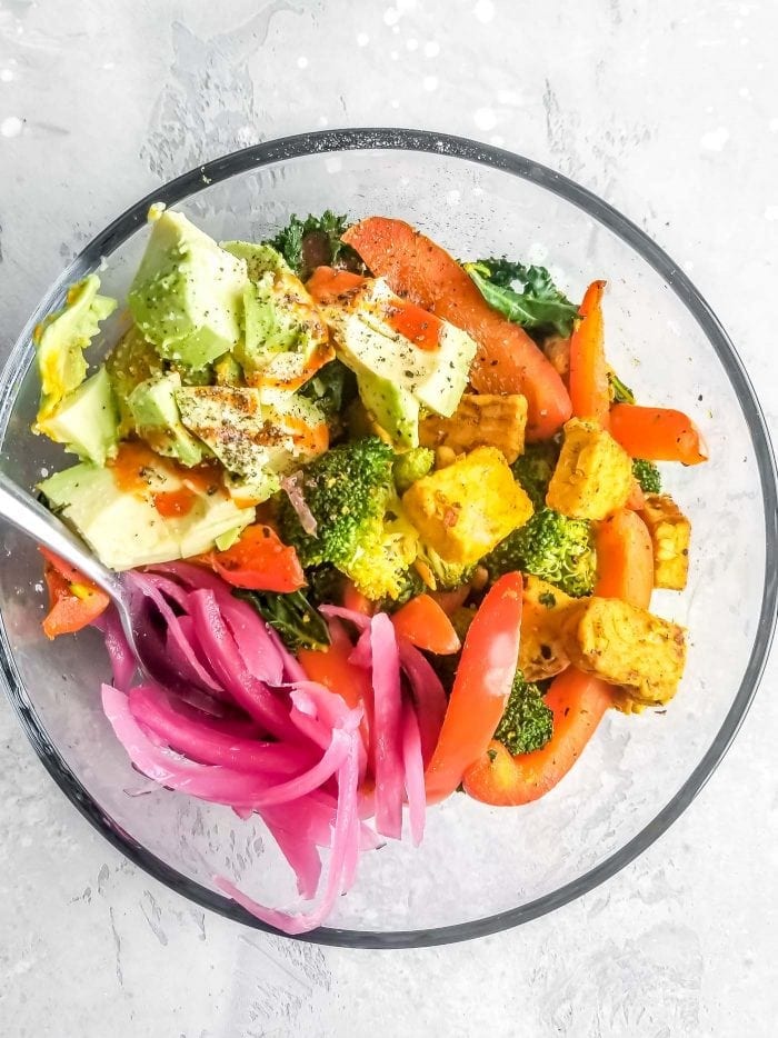 A bowl with broccoli, pickled onion, avocado and bell pepper.
