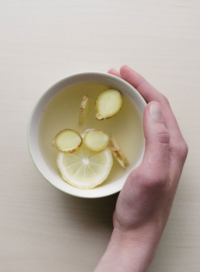Hand cupping a mug of tea with ginger and lemon in it.