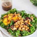 A kale salad topped with squash, chickpeas, cranberries, hemp seeds and walnuts.