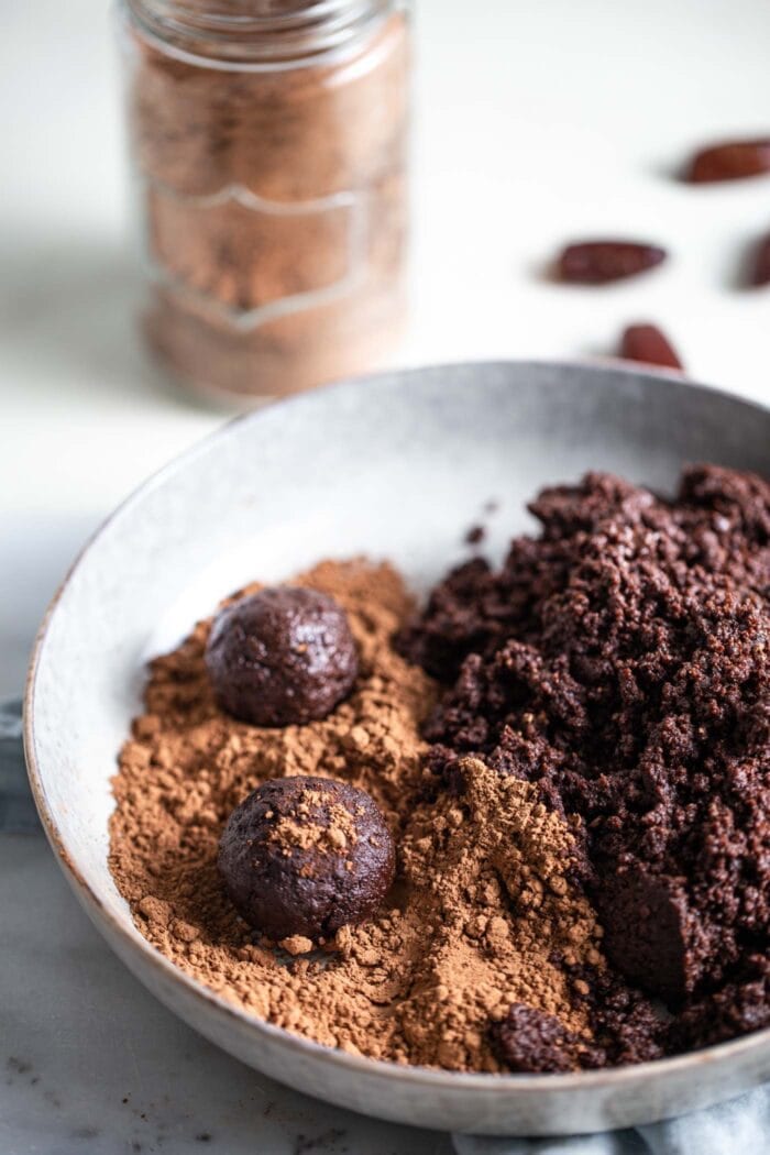 Chocolate date energy balls sitting on a plate being dusted with cocoa powder.