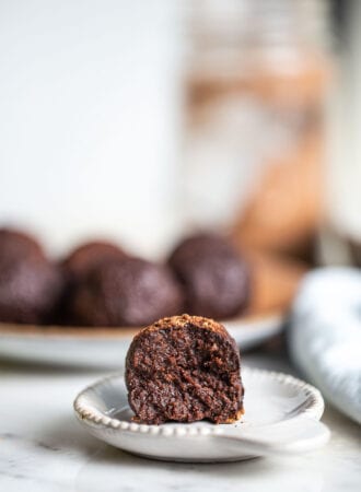 A tahini chocolate date ball with a bite taking out of it sitting on a small plate.