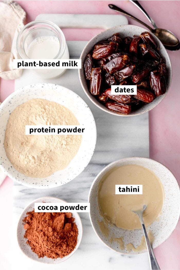 All the ingredients needed for making no-bake chocolate protein bars: tahini, cocoa powder, milk, dates and protein powder.