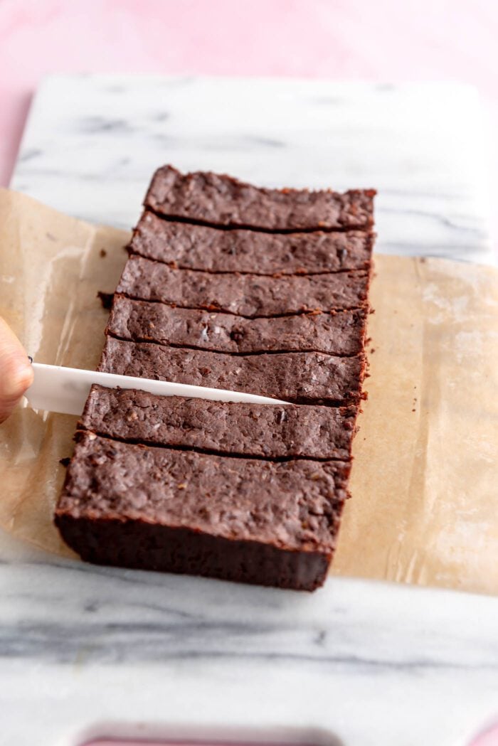 Knife slicing chocolate protein bars into 8 portions on a marble cutting bars.