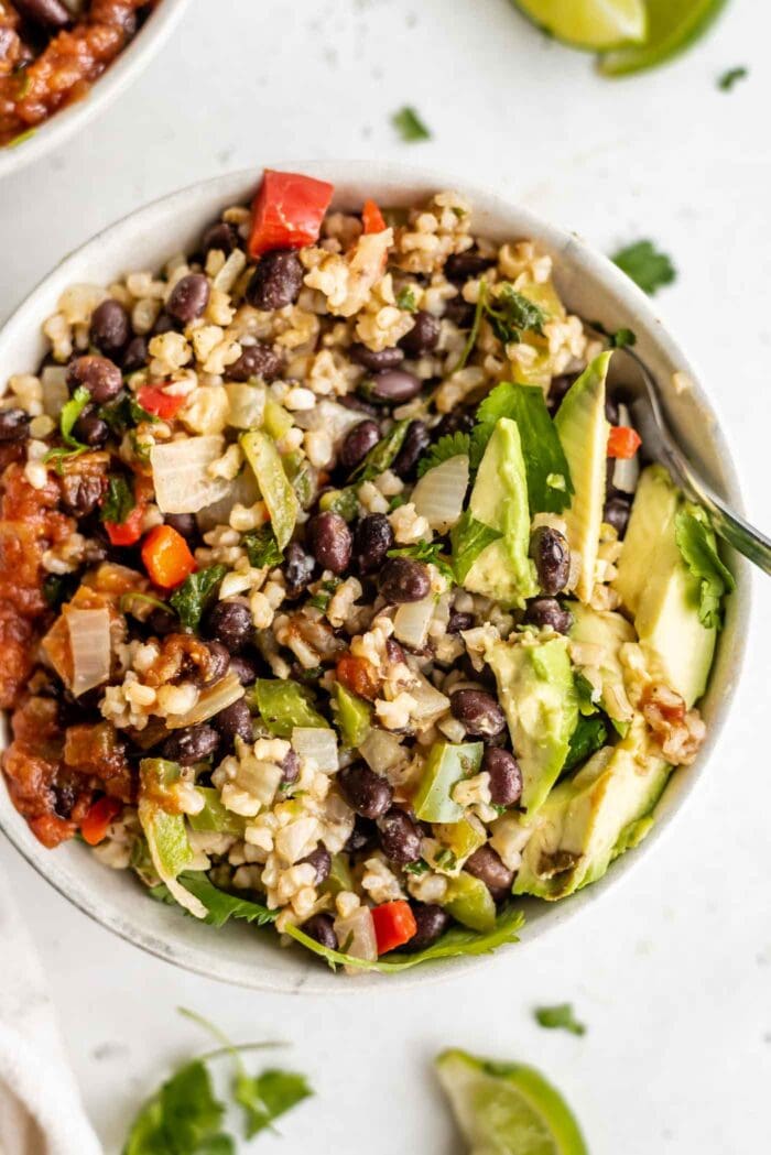 A bowl of rice and beans topped with avocado and salsa.