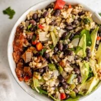 A bowl of rice and beans topped with avocado and salsa.