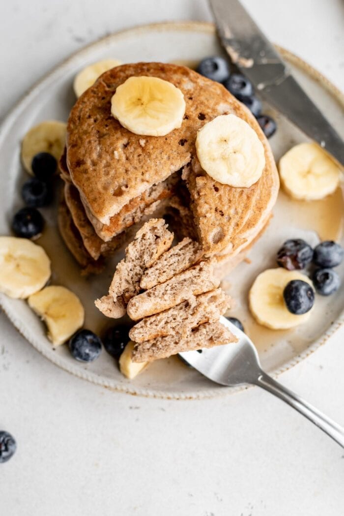 A sliced stack of blueberry and banana topped buckwheat pancakes on a plate.