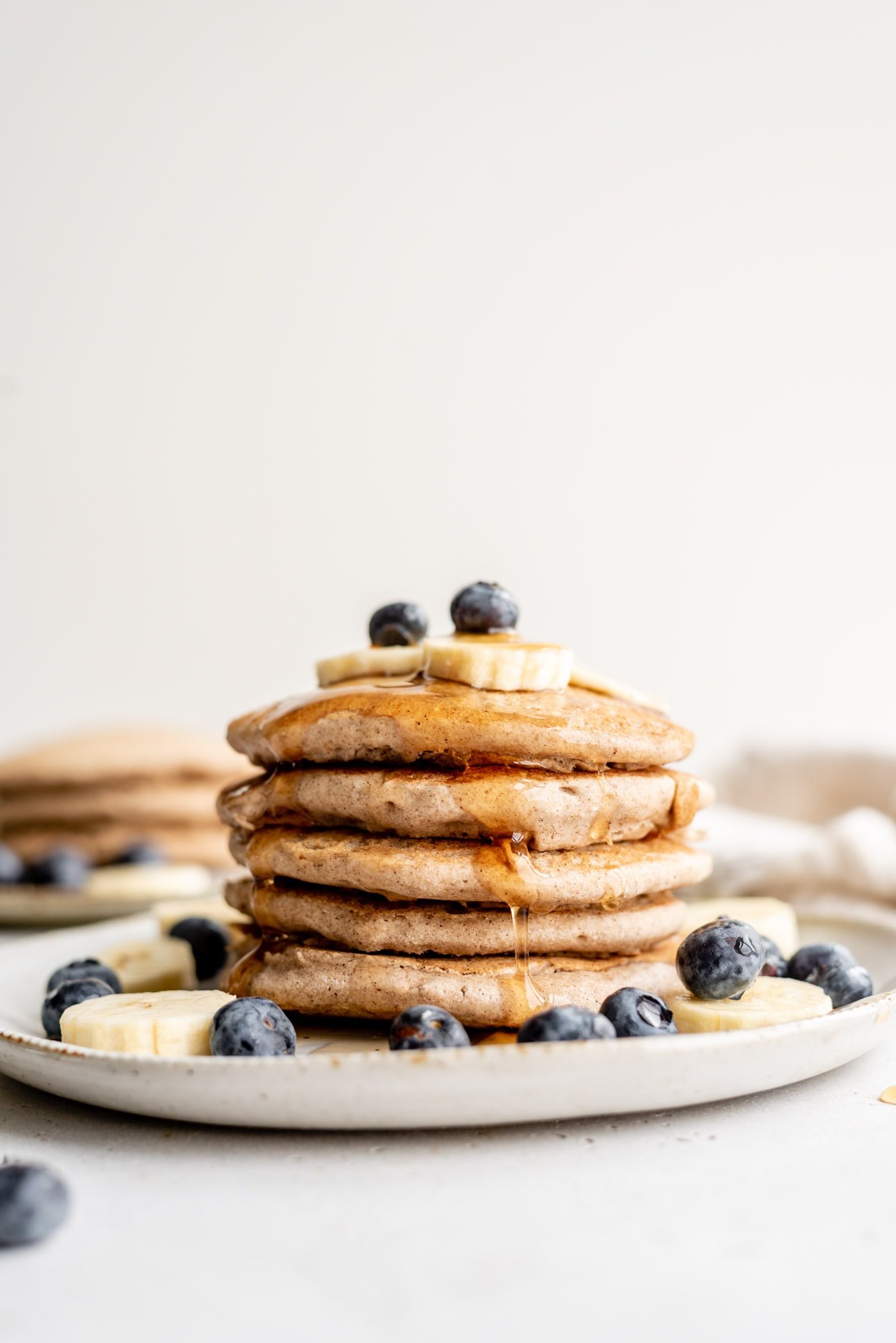 A stack of buckwheat pancakes on a plate, topped with blueberry, banana and syrup.