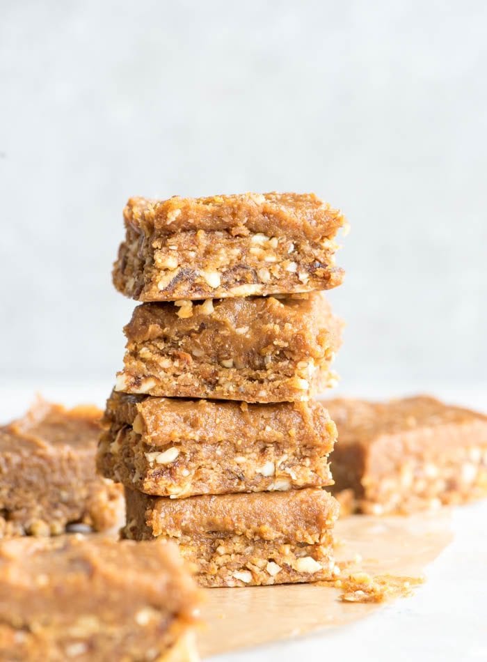 Stack of 4 peanut butter blondies with peanut butter frosting on a piece of parchment paper with a few more bars scattered around the background.