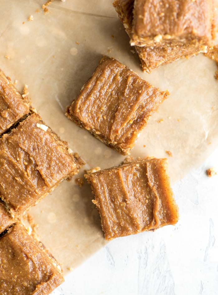 Overhead view of a few peanut butter blondies with peanut butter date frosting scattered around a piece of parchment paper.