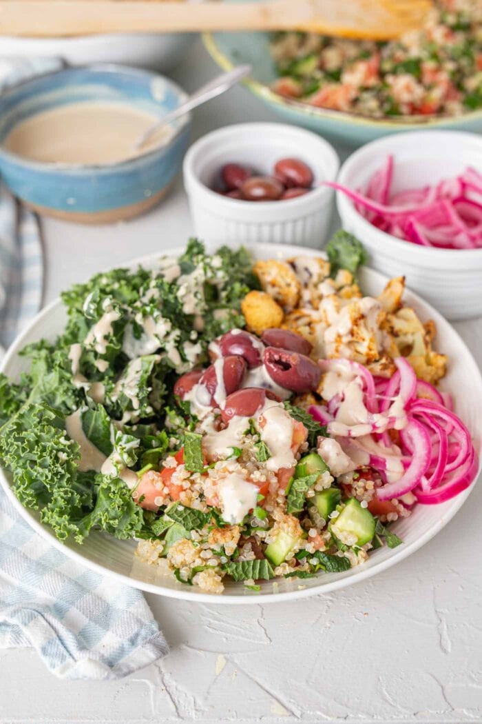 A bright bowl of healthy ingredients pickled onions, cauliflower, quinoa, kale and olives.
