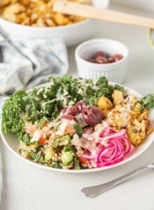 A bright bowl of healthy ingredients pickled onions, cauliflower, quinoa, kale and olives.