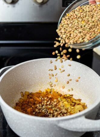 A dish of dry green lentils being dumped into a pot on the stovetop.