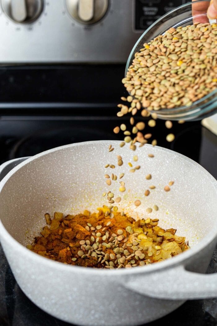 A dish of dry green lentils being dumped into a pot on the stovetop.