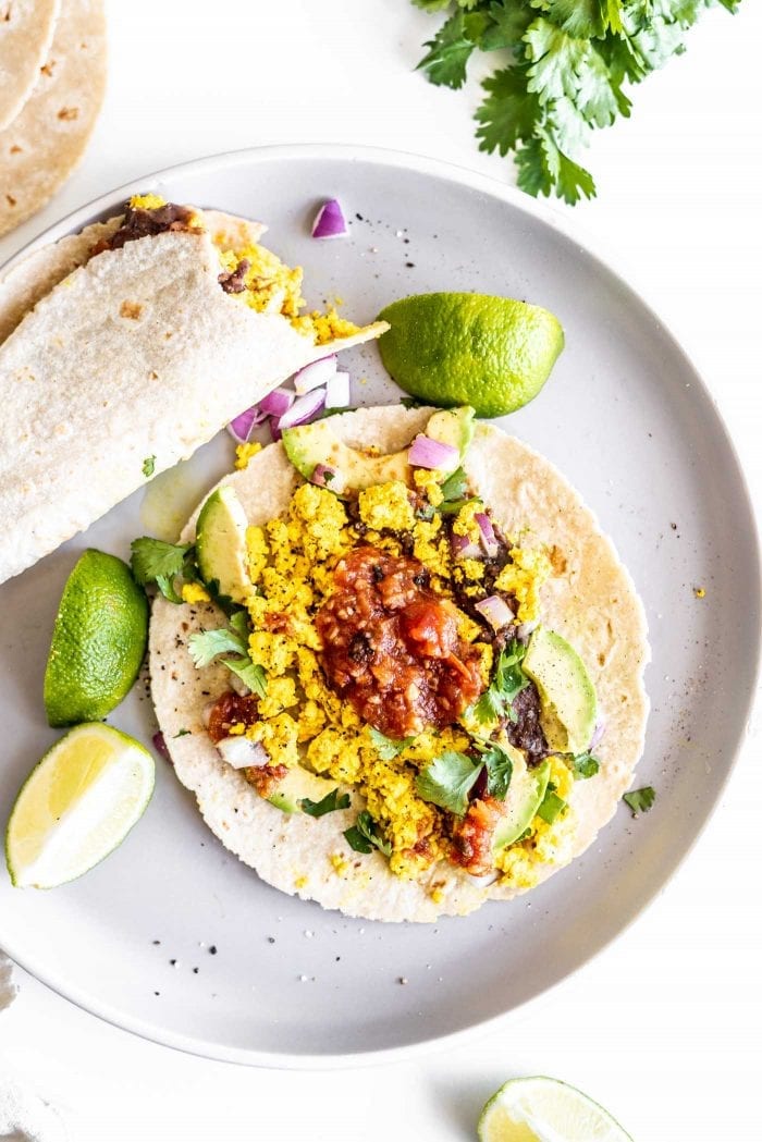 Two tofu scramble tacos with refried beans, lime, salsa and cilantro.