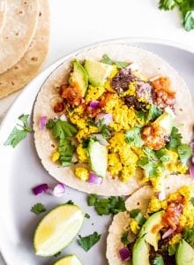 A stuffed vegan breakfast taco on a plate with cilantro, beans and avocado.