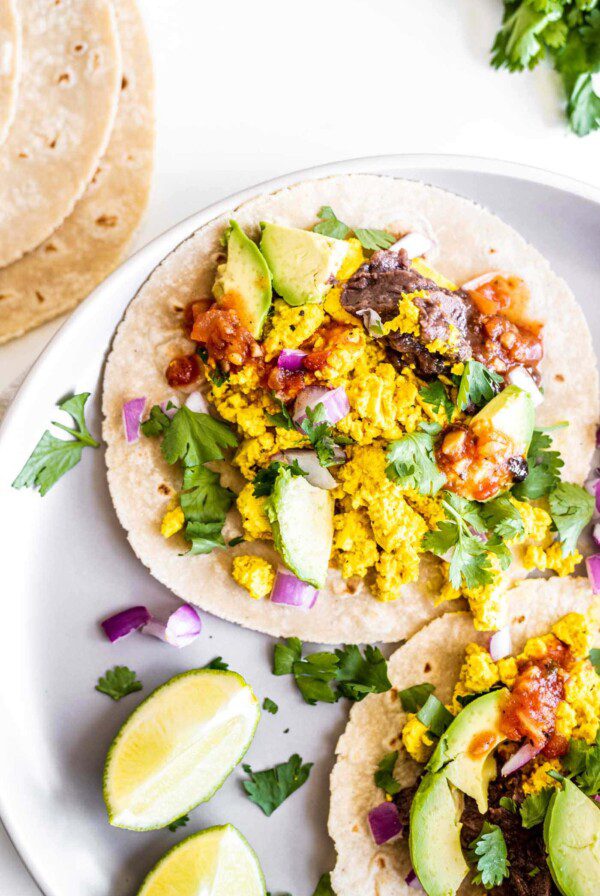 A stuffed vegan breakfast taco on a plate with cilantro, beans and avocado.