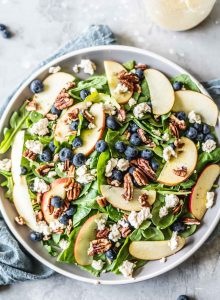 Spinach salad on a grey plate with blueberries, pecans, apple and tofu feta.