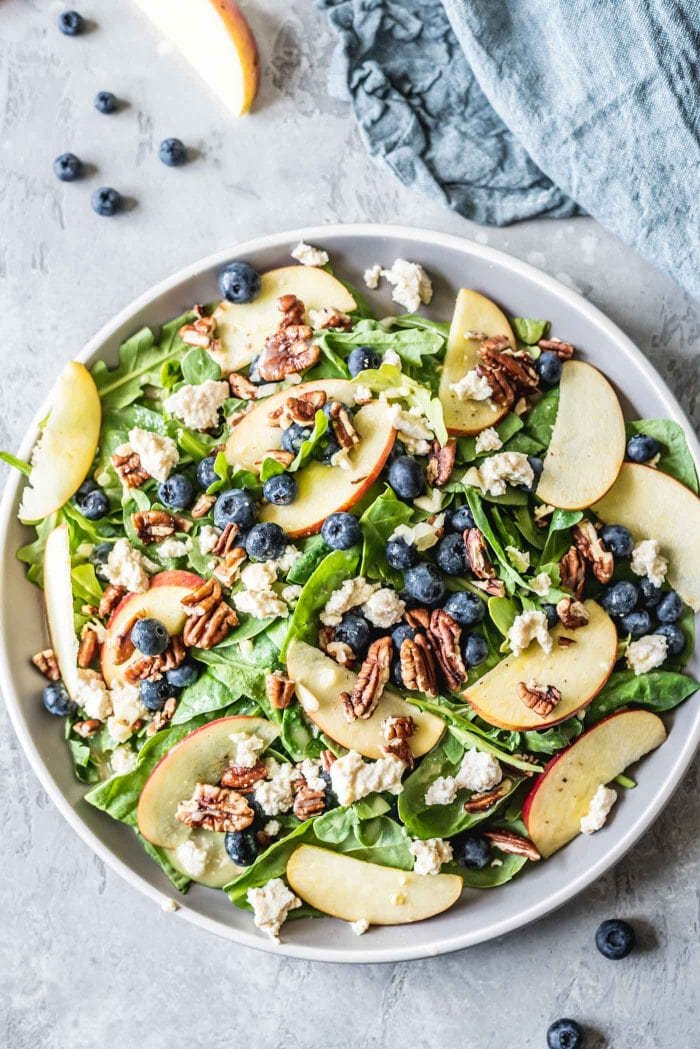 Green salad with blueberries, pecans, tofu feta and apple on a grey plate.