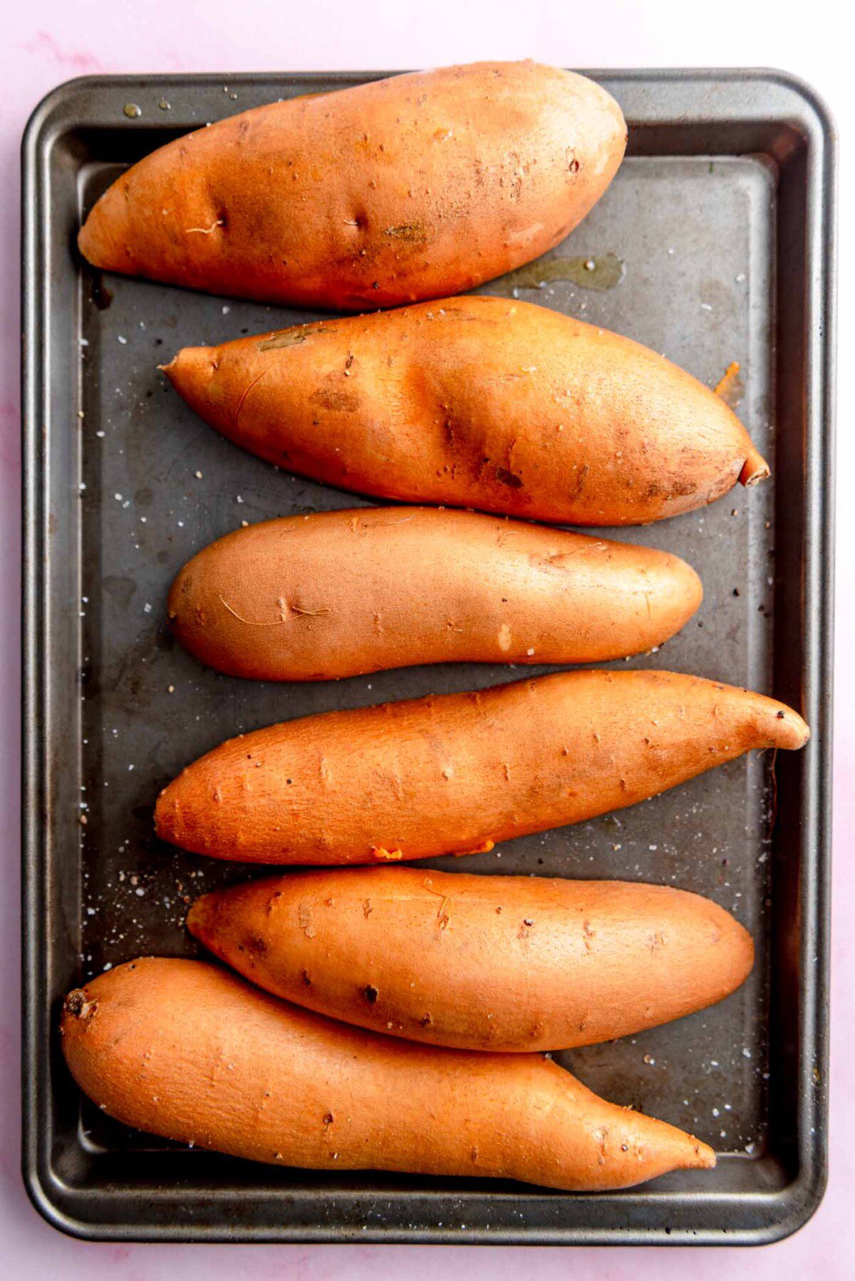 Sweet potatoes cut in half and placed cut side down on a baking sheet.