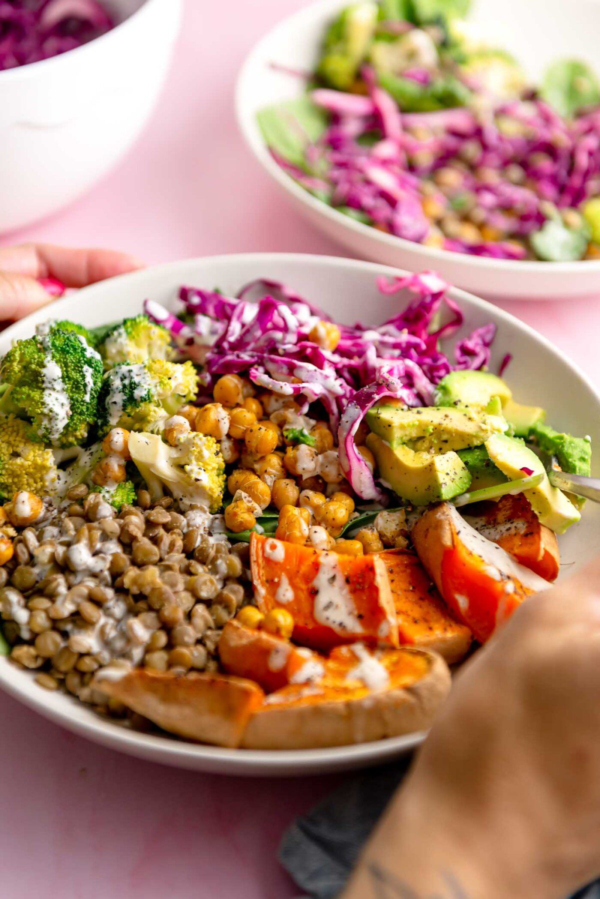 Bowl with sweet potato, avocado, shredded red cabbage, lentils, broccoli, chickpeas and a drizzle of tahini sauce.